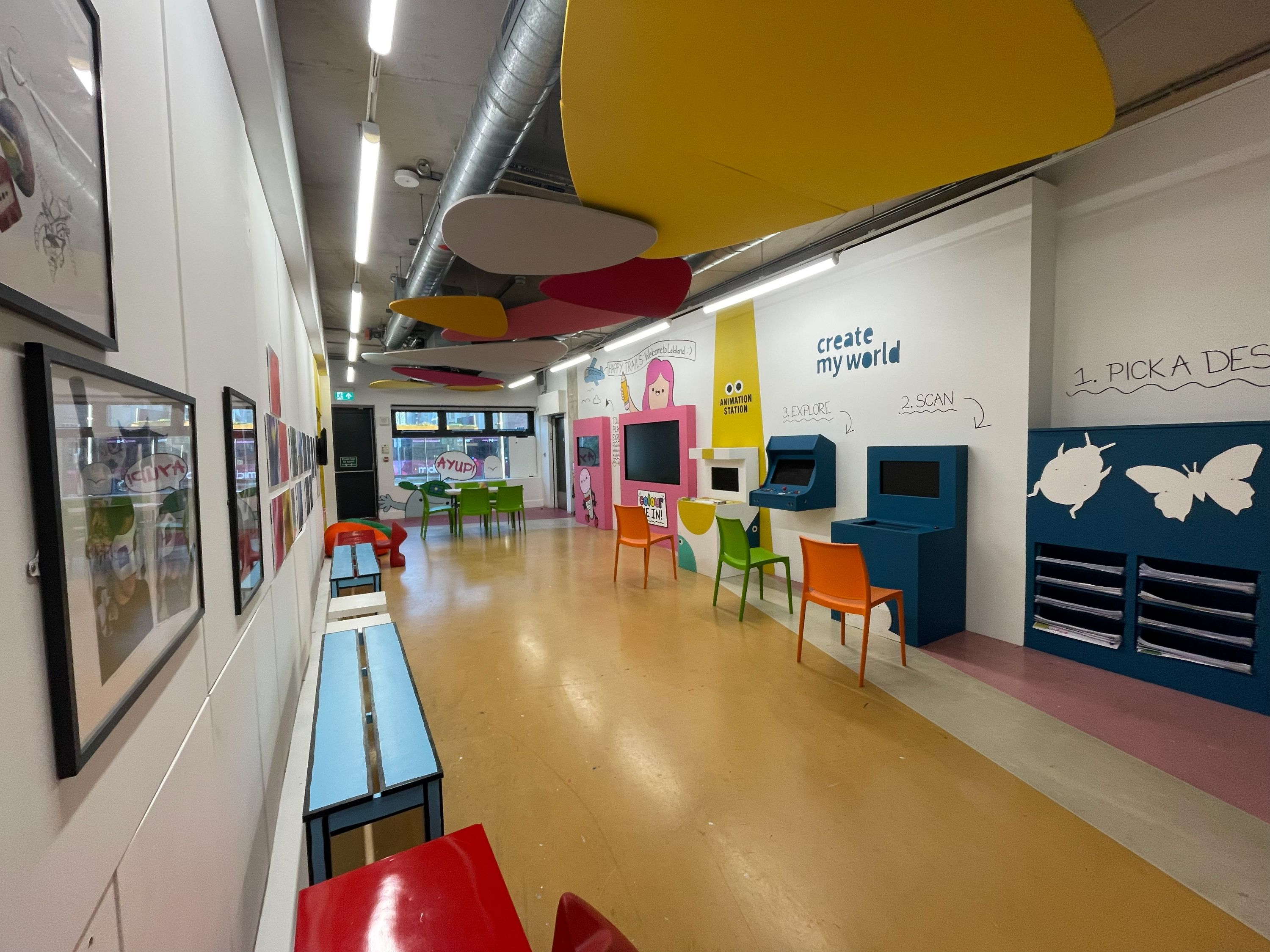A long, brightly decorated room containing activities for families, such as interactive screens