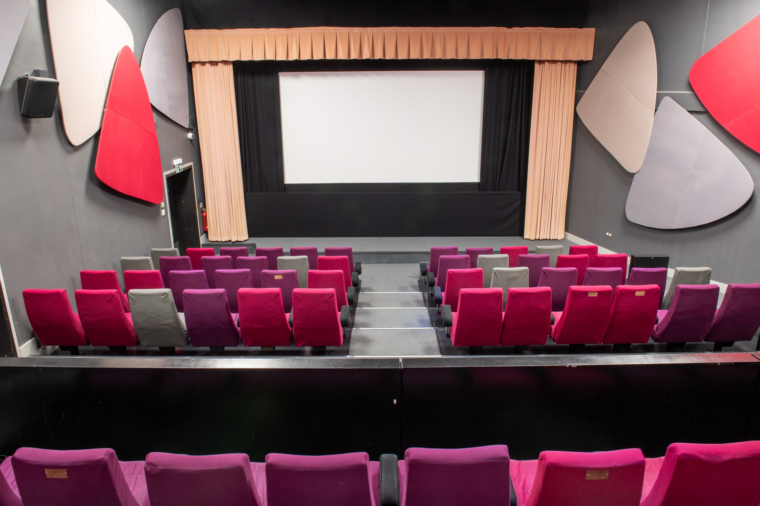 Image Credit: Jon Legge Rows of tiered purple, pink and grey cinema seating looking down towards a cinema screen